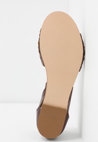 Chaussure en cuir marron avec un dessus texturé, semelle plate et semelle extérieure en caoutchouc beige clair, présentant des rainures pour la traction. Taille 37.