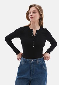 Schwarzer, gerippter Langarm-Body mit einem Henley-Ausschnitt und fünf Knöpfen. Kombiniert mit hoch taillierten blauen Jeans.