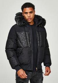 Giacca a vento nera con design trapuntato e cappuccio in pelliccia sintetica. Presenta chiusura con zip, texture a contrasto e polsini a costine.