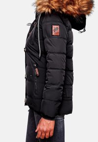 Zwarte pufferjack met een faux fur-gevoerde capuchon, gequiltte textuur, ritszakken en een embleem patch op de schouder.