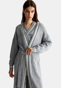 Accappatoio grigio a maglia con design avvolgente, caratterizzato da un motivo testurizzato, maniche ampie e accenti a righe grigie chiare e bianche lungo i bordi.
