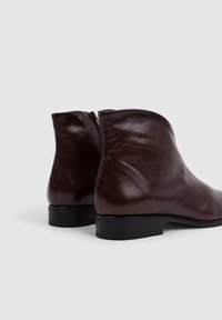 Bottines en cuir marron avec une finition lisse, dotées d'une fermeture éclair sur le côté, d'un bout arrondi et d'un petit talon noir.