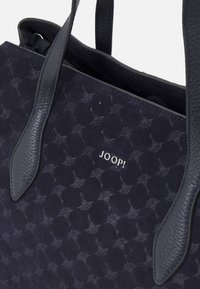 Granatowa torba na ramię zamszowa z teksturowanym wzorem, gładkimi skórzanymi uchwytami oraz srebrnym tłoczonym logo "JOOP!" na przodzie.