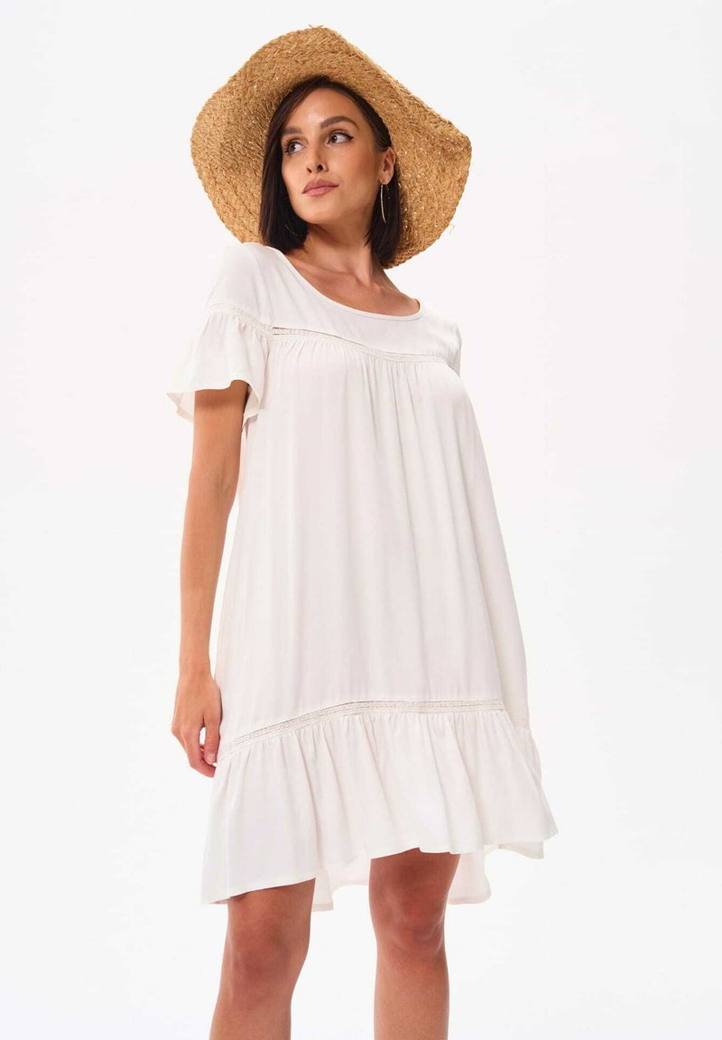 Witte A-lijn jurk met korte mouwen, geplooide details en een gerimpelde zoom. Gekozen in combinatie met een brede strohoed voor een casual look.