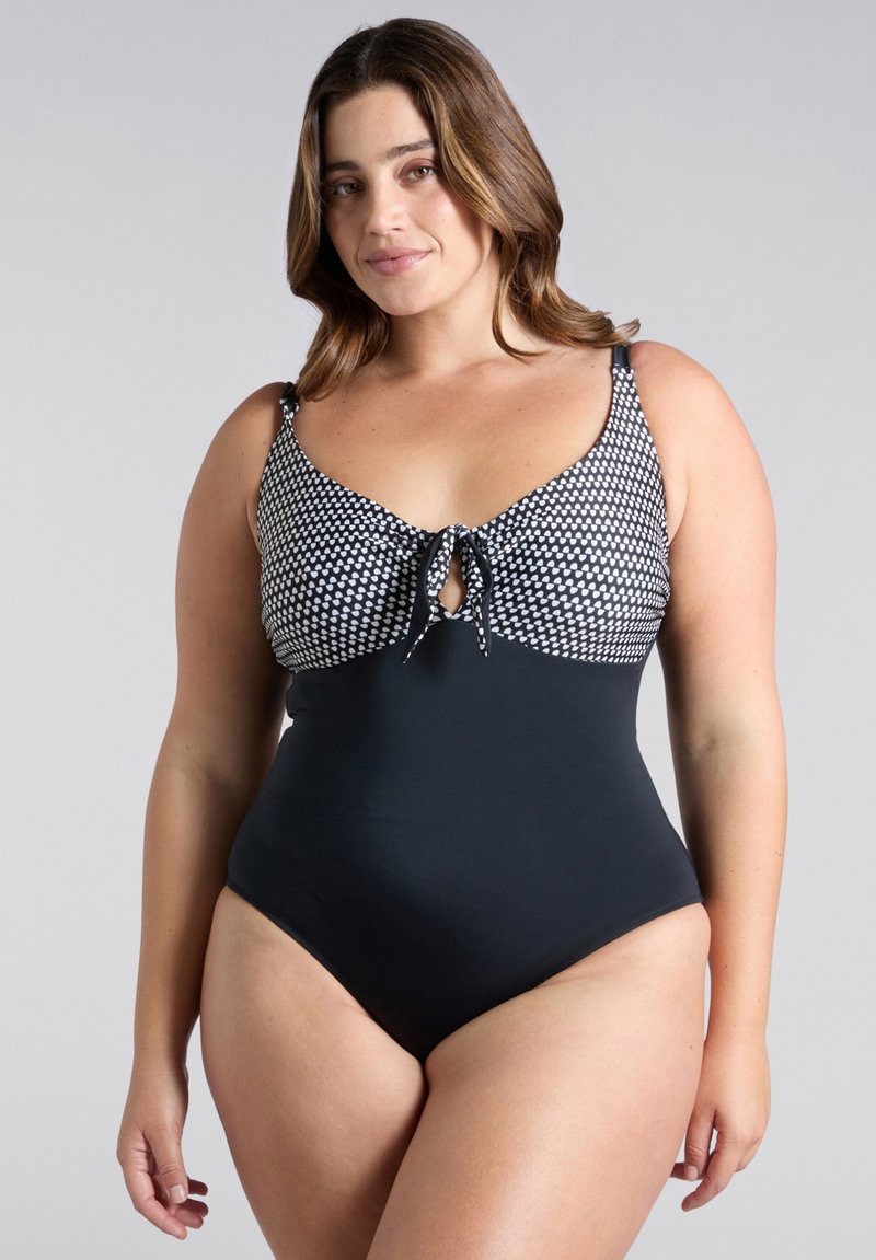 Mustavalkoinen kuvioitu yksiosainen uimapuku, jossa on solmittava etuosa, säädettävät olkaimet ja sujuva musta alaosa.