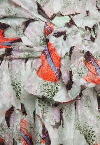 Multibarevná tkanina s abstraktními vzory v červené, zelené a modré. Textura vypadá mírně zvlněná s volným okrajem.