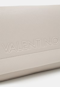 Light beige leather clutch with embossed "VALENTINO" logo, smooth texture, and subtle stitching details along the seam. Rectangular shape.