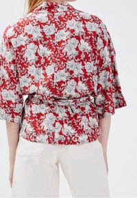 Red floral blouse with white and black floral patterns. Features short sleeves and a tied waist, made of lightweight fabric.