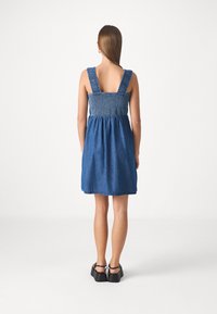 Vestido de mezclilla con un corsé fruncido, tirantes anchos y una falda acampanada. Color azul oscuro sólido, costuras mínimas y cremallera en la parte posterior.