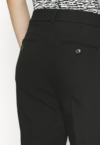 Černé kalhoty na míru s vysokým pasem, se dvěma zadními kapsami na knoflíky a jemnou strukturou.