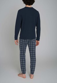 Top a maniche lunghe blu navy abbinato a pantaloni pigiama a quadri blu e grigi, con una vestibilità aderente e gambe affusolate. Il tessuto appare morbido e strutturato.