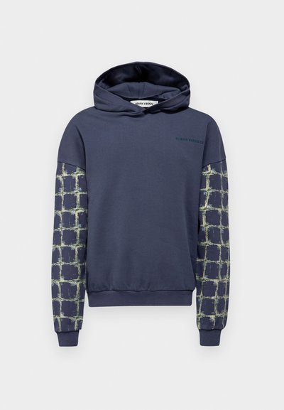 Námornícku mikinu s kapucňou, ktorá má prednú časť jednoliatej farby a rukávy so vzorom v geometrickej mriežke so zelenými akcentmi. Mäkká, textúrovaná látka.