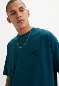 Tricou din bumbac de culoare teal, cu un logo negru "Levis" pe piept, guler rotund și mâneci scurte. Materialul pare neted, având o croială lejeră.