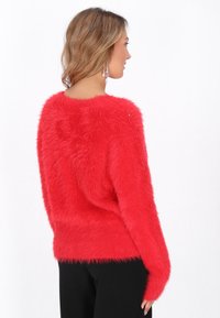 Pulover roșu pufoș cu o croială lejeră, guler rotund și mâneci lungi. Prezintă o țesătură texturată și accente decorative mici pe umăr.
