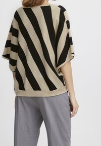 Sweter w paski w odcieniach beżu i czerni, z wyraźnymi ukośnymi liniami, miękką teksturą, szerokimi rękawami i luźnym krojem z tyłu.