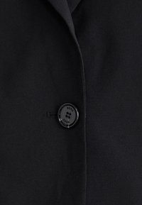 Black blazer fabric with a smooth texture, featuring a prominent black button labeled "BOSS" and a classic lapel design.