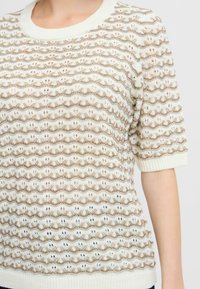 Suéter de punto con cuello redondo, que presenta un patrón de olas en beige y blanco, con mangas cortas y un acabado texturizado.