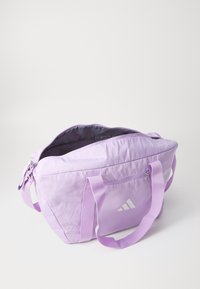 Ljubičasta platnena torba s dva ručka, s patentnim zatvaračem na vrhu i bočnom džepom. Sadrži Adidas logo u bijeloj boji s jedne strane. Glatka tekstura.