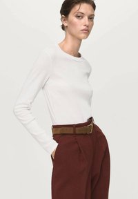 White long-sleeve top paired with high-waisted, dark burgundy trousers and a brown belt. Smooth fabric, simple design, and tailored fit.