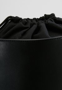 Musta nahkakäsilaukku, jossa on rypistetty kangaskansi, sileä päällinen ja teksturoitu, pehmeä nyörikansi.