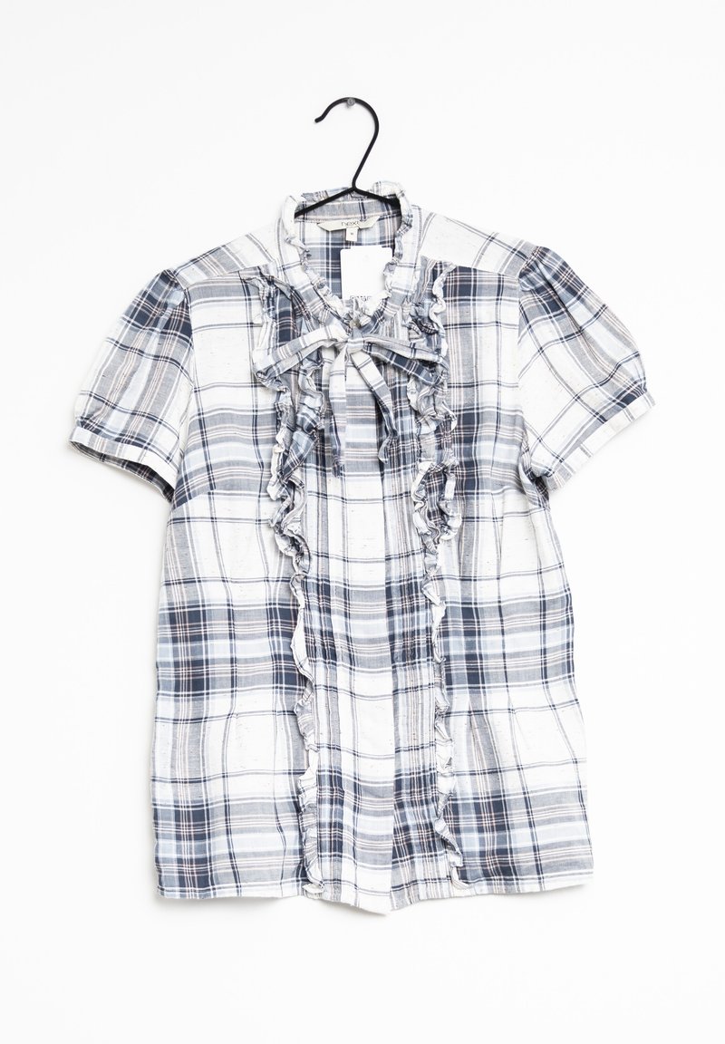 Blouse à manches courtes à carreaux avec devant froncé et col à nouer, suspendue sur un cintre noir.