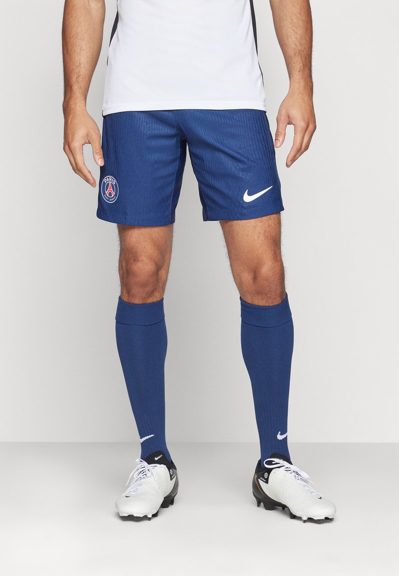 Siniset urheilushortsit, joissa on pystysuorat raidat ja Pariisi-logo. Yhdistettynä sinisiin sukkiin ja valkoisiin jalkapallokenkiin, joissa on Nike-brändäys.