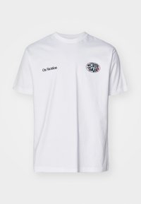 T-shirt de algodão branco com mangas curtas, decote redondo, texto preto "Em Férias" e um gráfico colorido "World Tour" no peito.