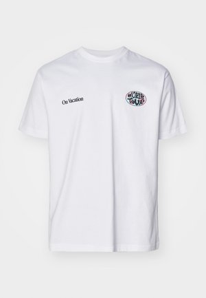 T-shirt en coton blanc avec des manches courtes, un col rond, le texte noir "En Vacances" et un graphique coloré "Tour du Monde" sur la poitrine.