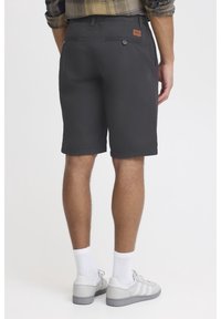 Shorts gris foncé avec une coupe décontractée, dotés de poches arrière et d'une étiquette en cuir. Associés à des chaussettes blanches et à des sneakers grises.