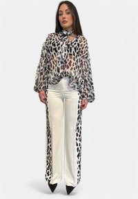 Blusa leggera e trasparente con stampa leopardata, dotata di maniche a volant e cravatta al collo; abbinata a pantaloni bianchi a gamba larga con dettagli leopardati laterali.
