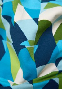 Nahaufnahme eines Stoffes mit abstraktem geometrischem Muster in Blau-, Marine-, Grün-, Hellblau- und Weißtönen.