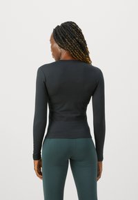 Svart, langermet topp laget av et glatt, elastisk stoff, med en enkel, rund halslinje og tettsittende silhuett, iført med grønne leggings.