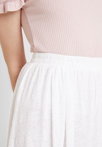 Ljusrosa ribbad topp ihop med en vit kjol med elastisk midja, med mjukt tyg som har en lätt textur och avslappnade veck.