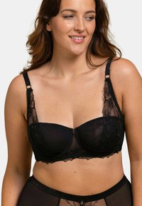 Soutien-gorge noir avec des détails en dentelle, soutien-gorge à armatures et bretelles réglables. Il présente une superposition en maille et des accents décoratifs près des bretelles.