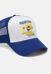 Blå og hvit trucker caps med mesh-paneler, med grafisk design av matvarer og tekst i gult. Bøyd skjerm og justerbar stropp.