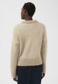Pull beige en maille avec une ceinture et des poignets côtelés, présentant une texture douce et pelucheuse ainsi qu'un col classique.