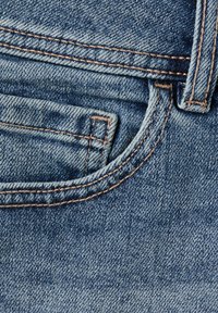 Gros plan sur un tissu en denim bleu montrant des coutures détaillées, une petite poche avant et une passants de ceinture sur un jean.