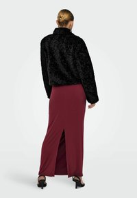 Sort faux fur jakke med krave parret med en rød, tætsiddende maxinederdel med en sideslids, båret med sorte hæle sandal.