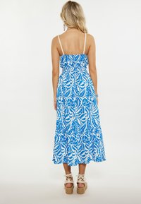 Rochie maxi cu imprimeu floral albastru și alb, cu bretele ajustabile tip spaghetti, cu bust volanat, talie elastică și fustă în straturi. Sandale cu toc wedge.