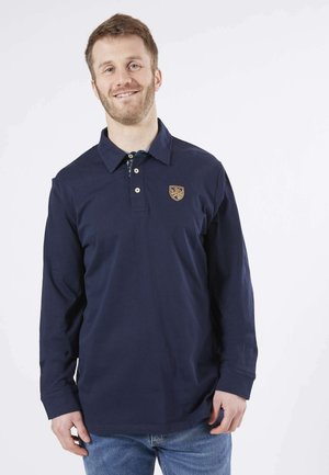 Polo-shirt à manches longues bleu marine avec une patte de boutonnage à trois boutons, logo brodé sur la poitrine et col classique ; associé à un jean bleu clair.