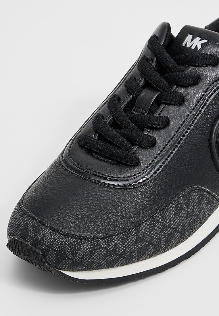 Zwarte leren en stoffen sneaker met zwarte veters, textuurpatroon op de neus, witte zool en "MK" logo op de tong.