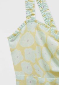 Robe jaune clair ornée d'un motif floral en vert menthe avec des centres violets ; des bretelles élastiques à volants sont visibles en haut.