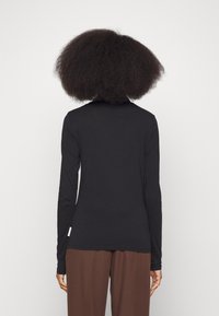 Schwarzes langärmliges Oberteil aus weichem Stoff, mit schlichter Gestaltung und figurbetonter Passform. Hinweis: Etikett ist an der linken Seite sichtbar.