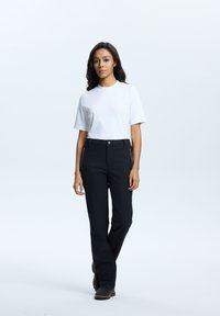 Hvid kortærmet t-shirt parret med sorte bukser med lynlåslommer. Modellen har mørke sko på, sat mod en lys baggrund.