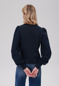 Sweatshirt bleu marine avec des manches bouffantes, un col rond et une taille cintrée. Le tissu semble doux et texturé.