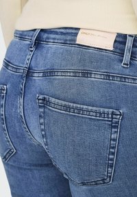 Tamno plavi traperice od denima s glatkom teksturom, sadrže dva stražnja džepa, suptilno izblijedile i oznaku s natpisom "ONLY Blue Denim."