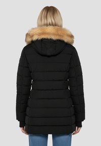 Doudoune noire avec texture matelassée horizontale, dotée d'une capuche amovible doublée de fourrure beige et de manches longues, vue de dos.