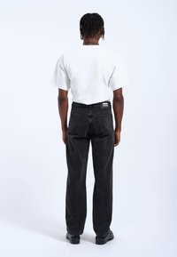 Vaqueros de mezclilla negra con corte recto y cinco bolsillos, combinados con una camiseta blanca de manga corta. Ambas prendas presentan un diseño minimalista.