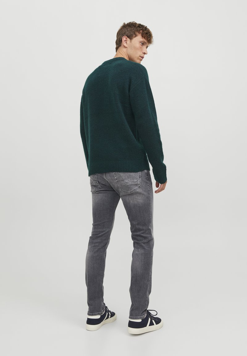 Suéter de lana de color verde oscuro con un corte relajado, combinado con jeans grises ajustados y zapatillas navy. El suéter tiene un dobladillo y puños acanalados.