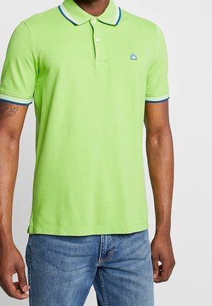 Homme portant un polo manches courtes vert citron avec un col et des bords de manches rayés bleu et blanc, associé à un jean bleu.